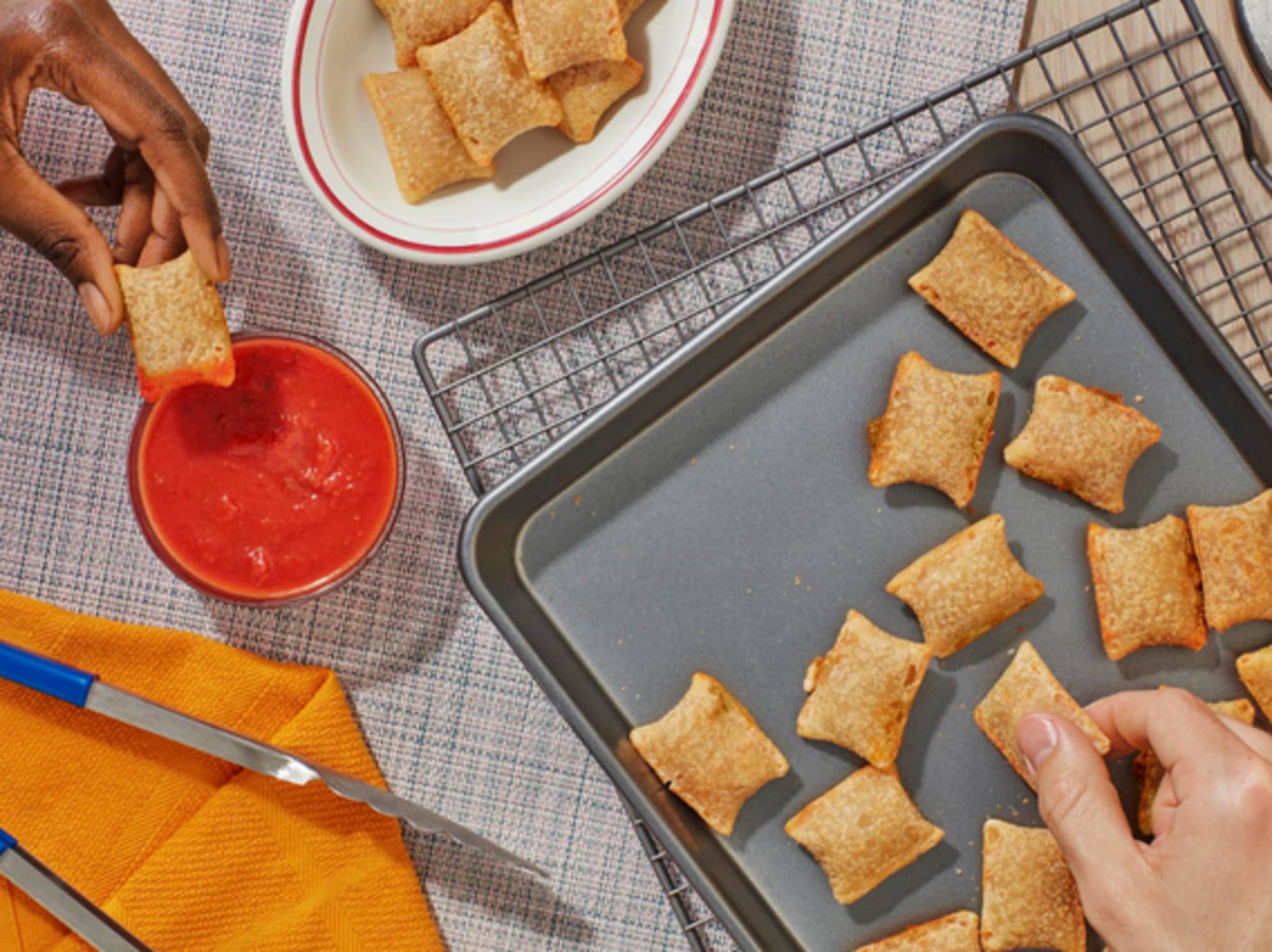 Totinos pizza rolls being taken off a baking sheet and dipped in marinara sauce